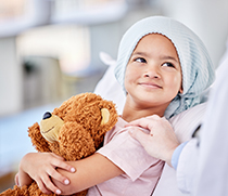 Krebskrankes Kind mit einem Teddy im Arm